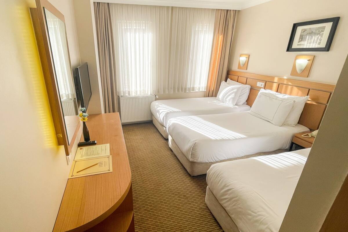 A hotel room with two beds, a wooden desk, a mirror, and a radiator.