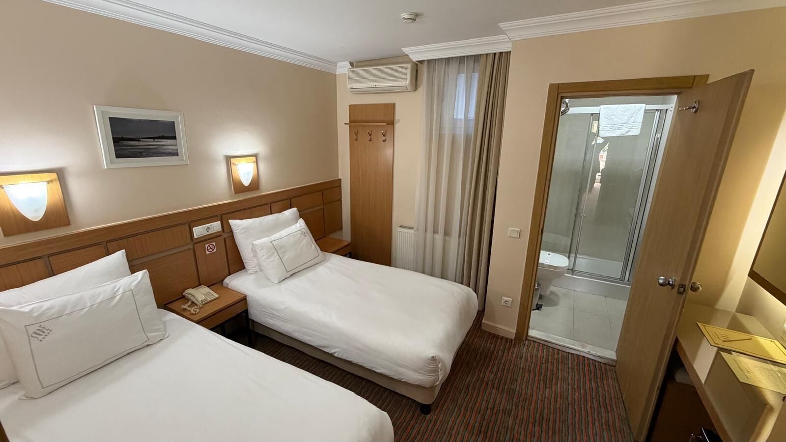 A hotel room with two beds, a bathroom, and a sliding glass door to the shower area.