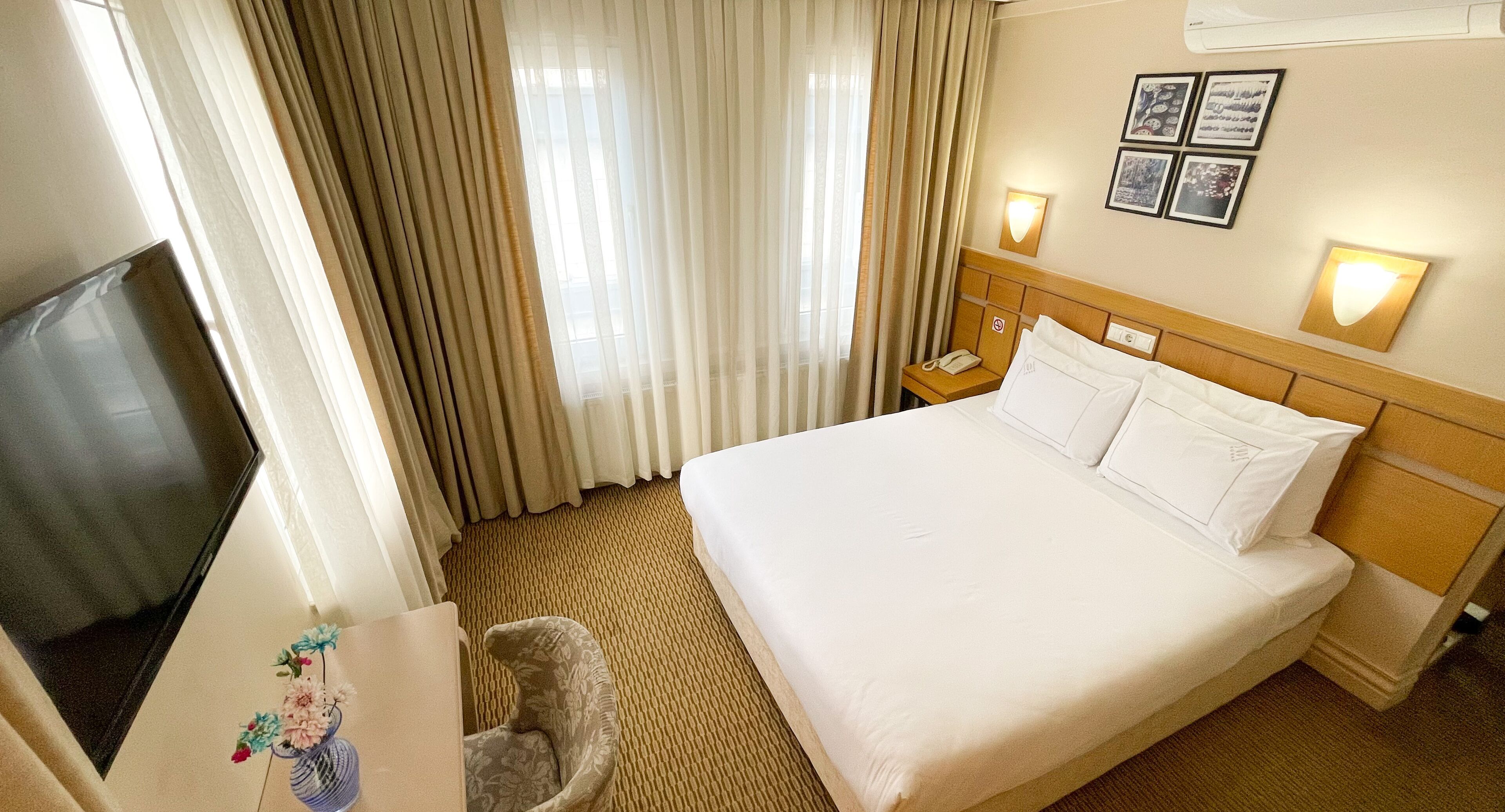 A hotel room with a large bed, a desk with a chair, a TV, and a window with curtains.