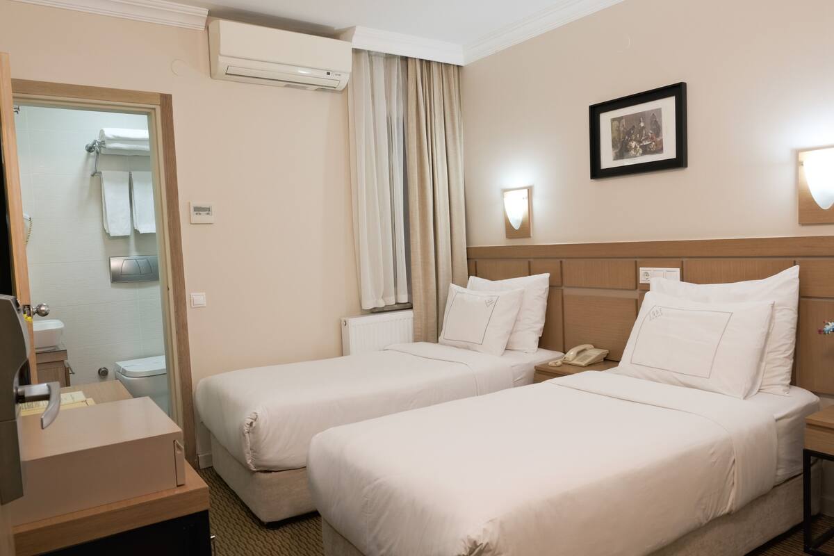 A hotel room with two beds, a bathroom, a desk with a telephone, and a framed picture on the wall.