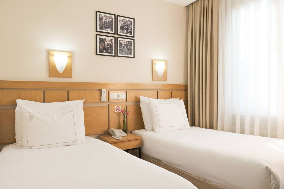 A hotel room with two beds, a wooden headboard, bedside tables with lamps, a phone, and a no-smoking sign.