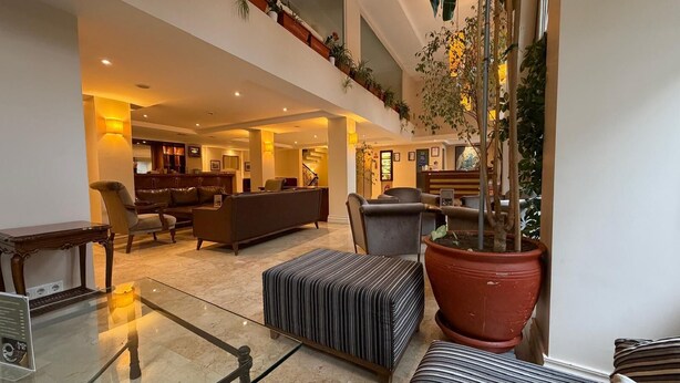 A spacious lobby with a high ceiling, a central seating area with sofas and chairs, a large potted plant, and a staircase leading to an upper level. - Sude Konak Hotel - Special class (Istanbul)