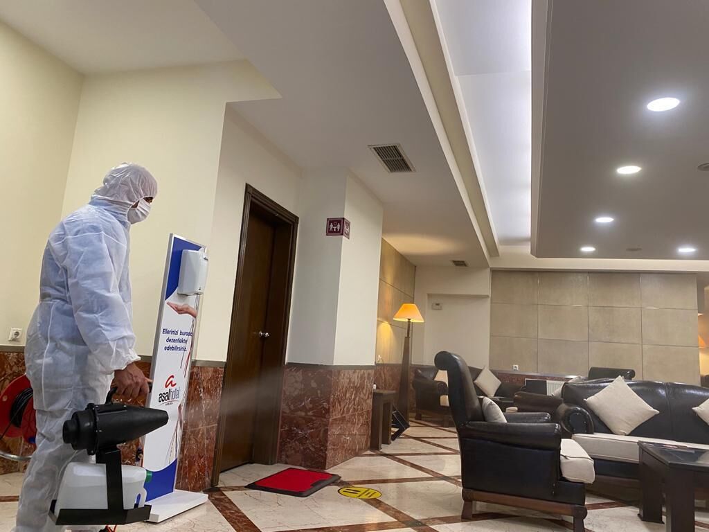 A hotel lobby with a seating area, a reception desk, and a person in protective gear.