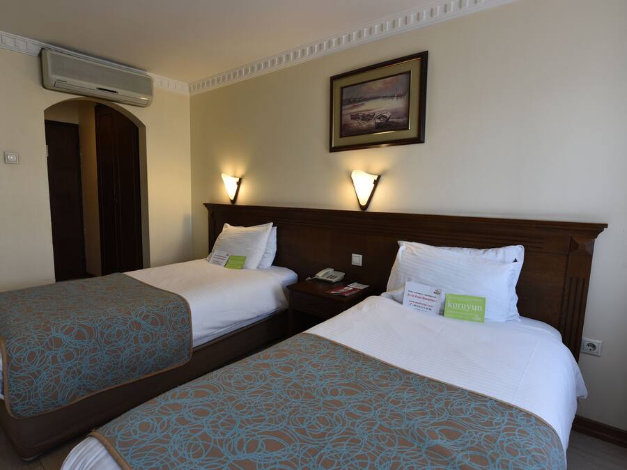 A hotel room with two beds, each with patterned bedding, a nightstand with a phone, and wall-mounted lights.