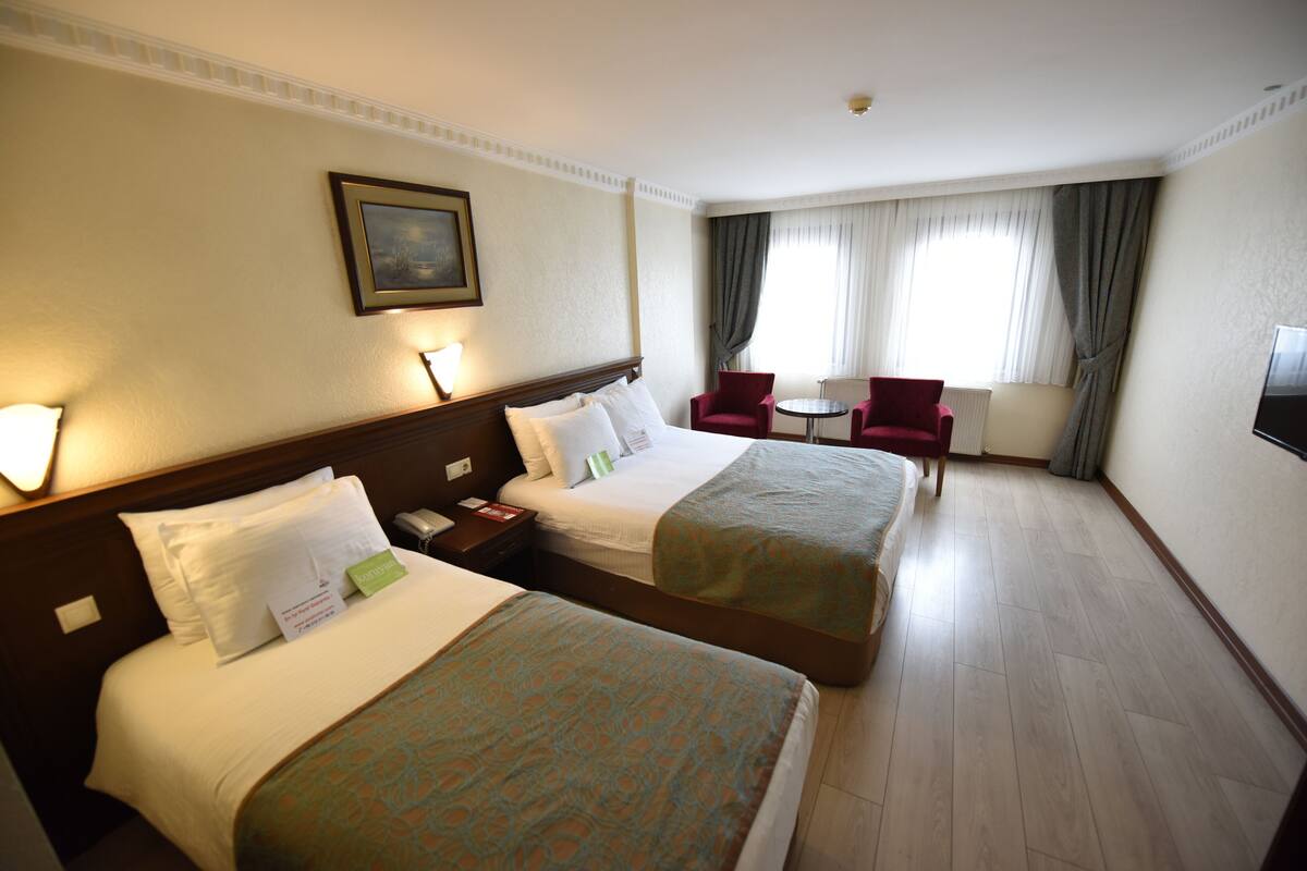 Habitación de hotel con dos camas, un escritorio, una silla, una mesita y un televisor.
