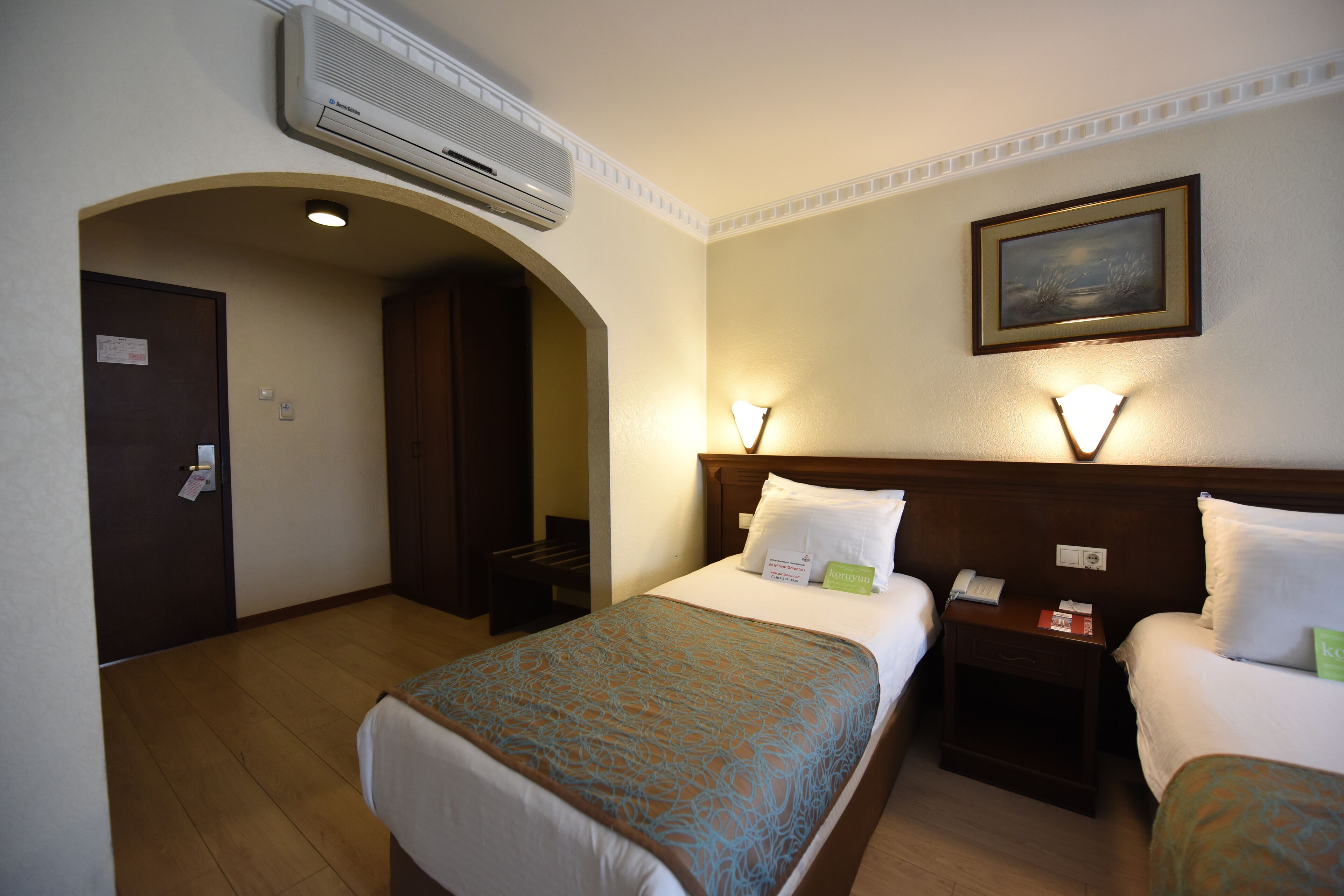 A hotel room with two beds, an air conditioner, a painting on the wall, and a door with a sign.