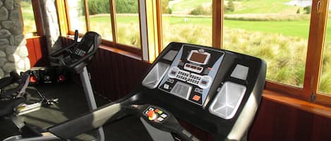 Un gimnasio con caminadora y máquina elíptica, ventanas amplias con vista a un campo de golf.