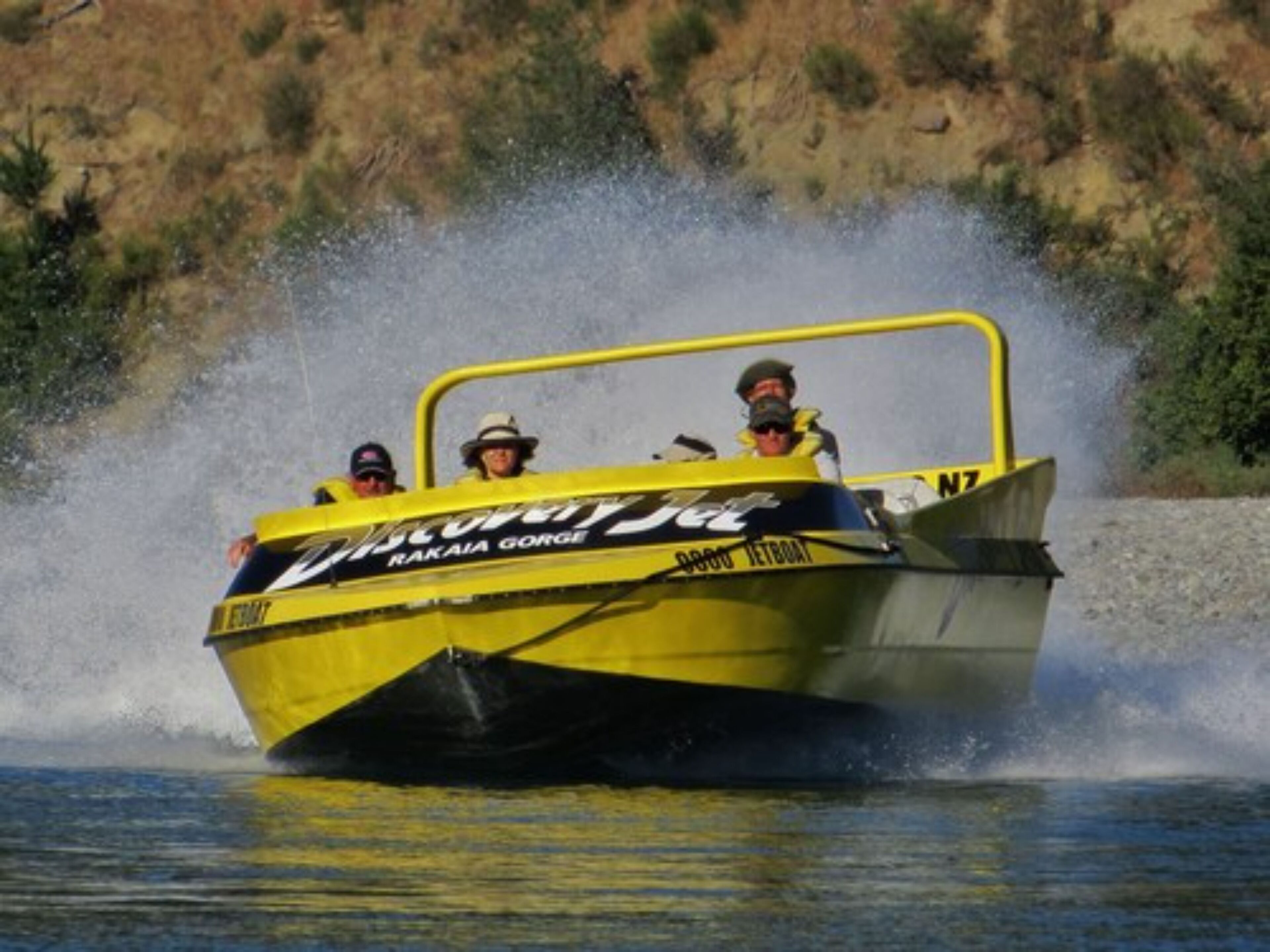 Una lancha amarilla y negra con el texto "RAKAIA GORGE" y "JETBOAT" en su lateral, deslizándose por el agua y levantando un salpico.