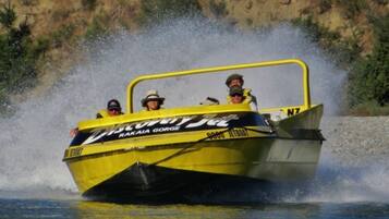 Una lancha amarilla y negra con el texto "RAKAIA GORGE" y "JETBOAT" en su lateral, deslizándose por el agua y levantando un salpico.