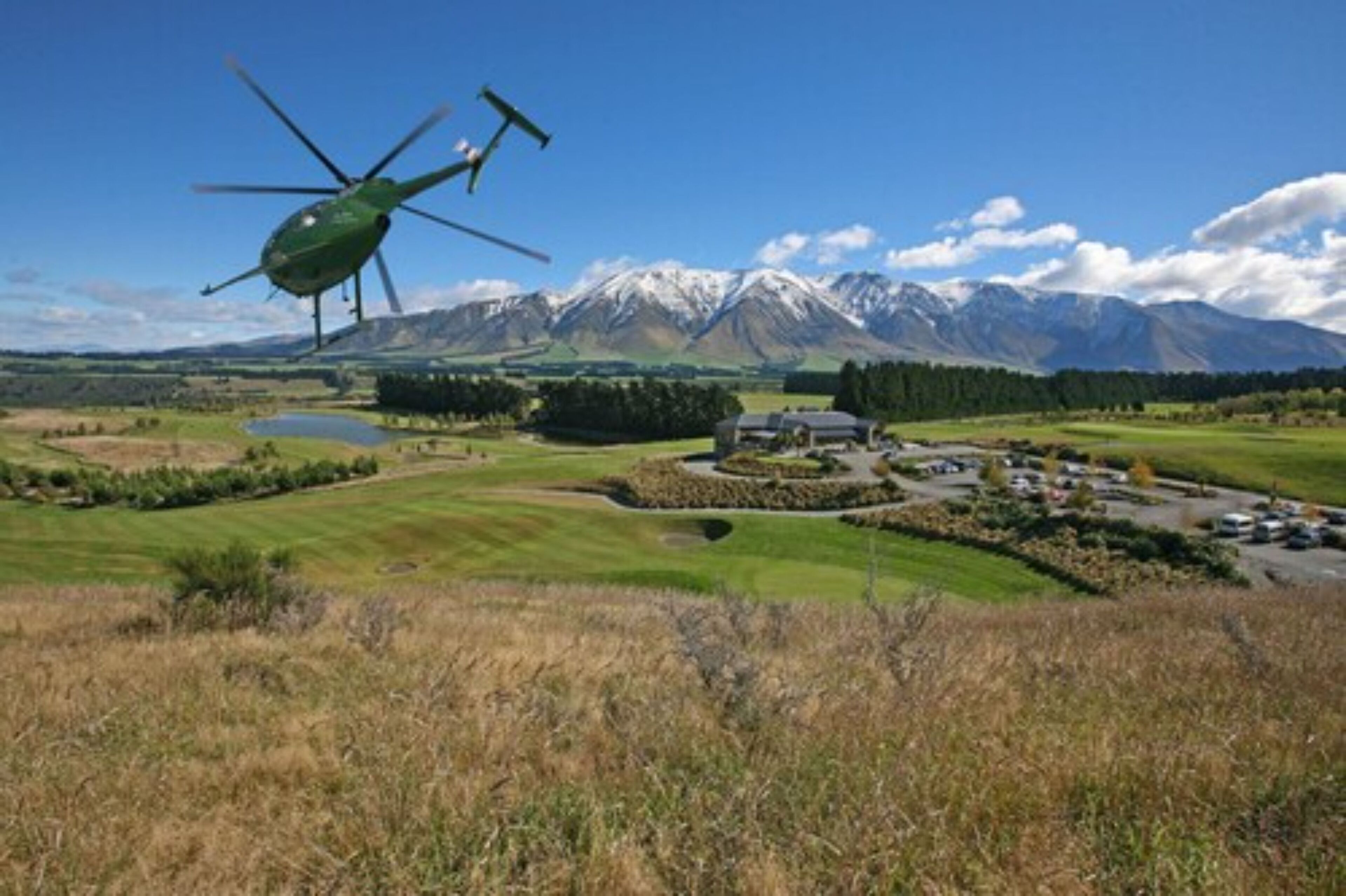 Un helicóptero volando sobre un paisaje con montañas, un campo de golf y un edificio.