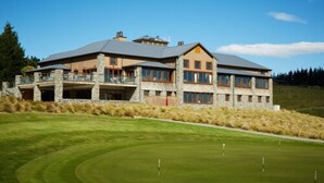 A large, multi-story building with a stone facade and multiple windows, situated on a well-maintained lawn with a golf course in the background. - Fable Terrace Downs Resort by Mgallery (Windwhistle)