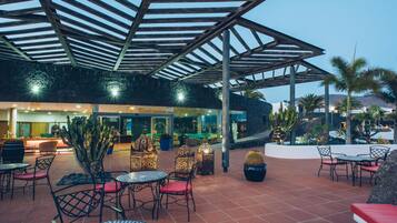 An outdoor patio area with tables and chairs, a covered seating area, and a reception desk.