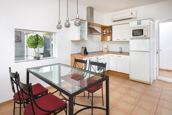Una cocina moderna con una mesa de comedor de vidrio, sillas rojas y un amplio ventanal con una planta.