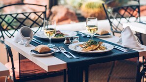 Une table à manger dressée avec des assiettes remplies de nourriture, des verres de vin blanc et des couverts.