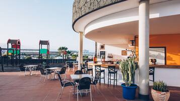Terraza al aire libre con mesas, sillas, zona de bar y plantas en macetas.