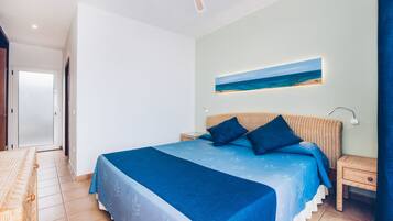 A bedroom with a large bed, a nightstand, a wall-mounted painting, and a door leading to another room.
