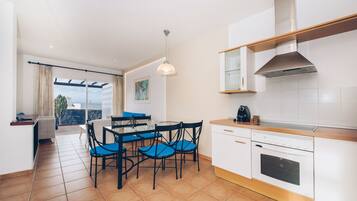 A modern kitchen with white cabinets, a built-in oven, and a dining area with blue chairs.