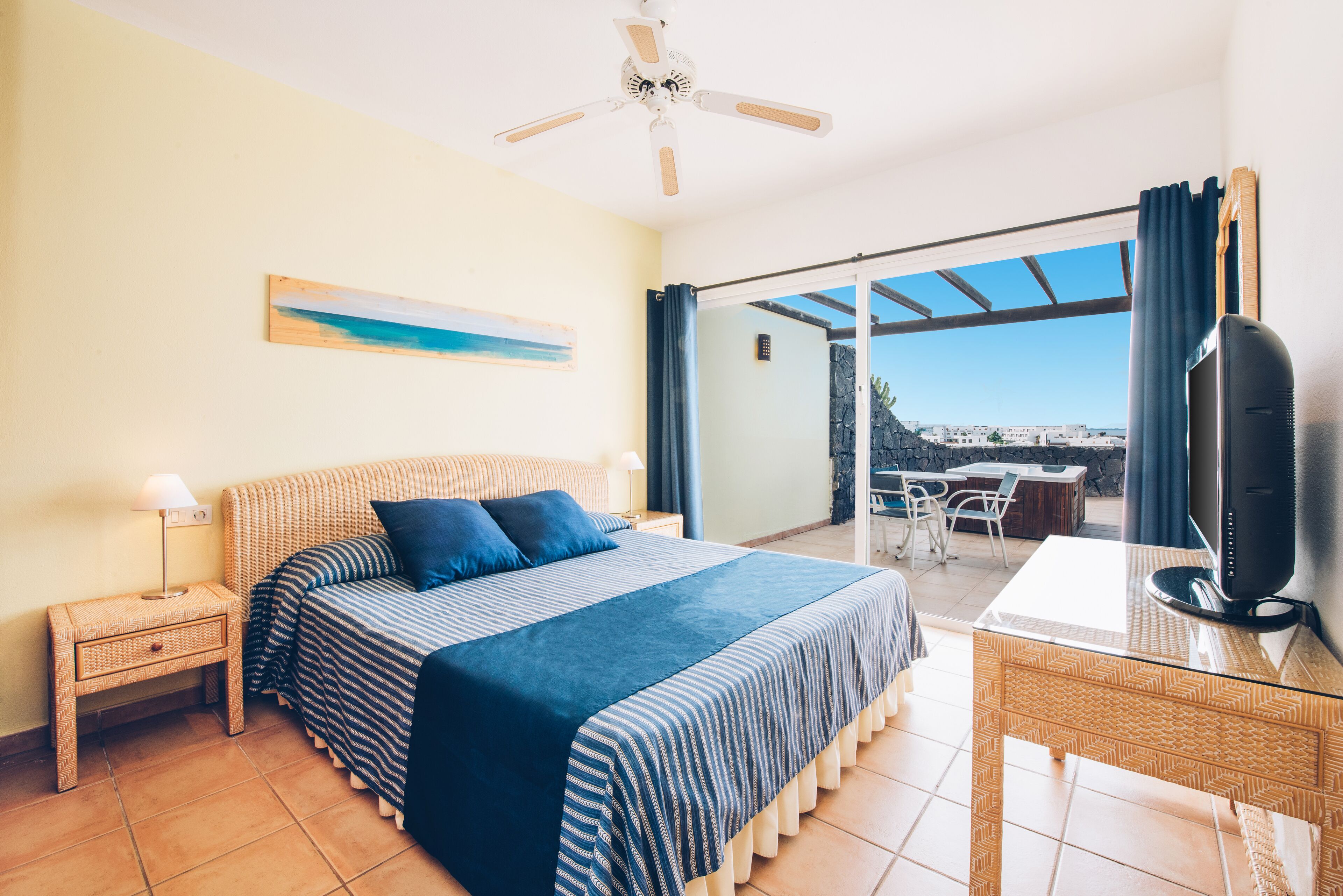Un dormitorio con cama, televisor, escritorio y vistas al exterior.