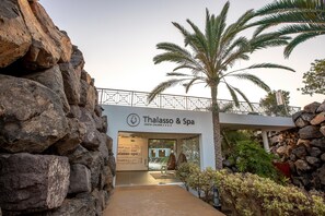 L’entrée du centre Thalasso & Spa est marquée par un mur de pierre et des palmiers.