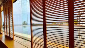 Un couloir doté de stores en bois à lamelles, d’un mur en verre et offrant une vue sur une piscine et un paysage.