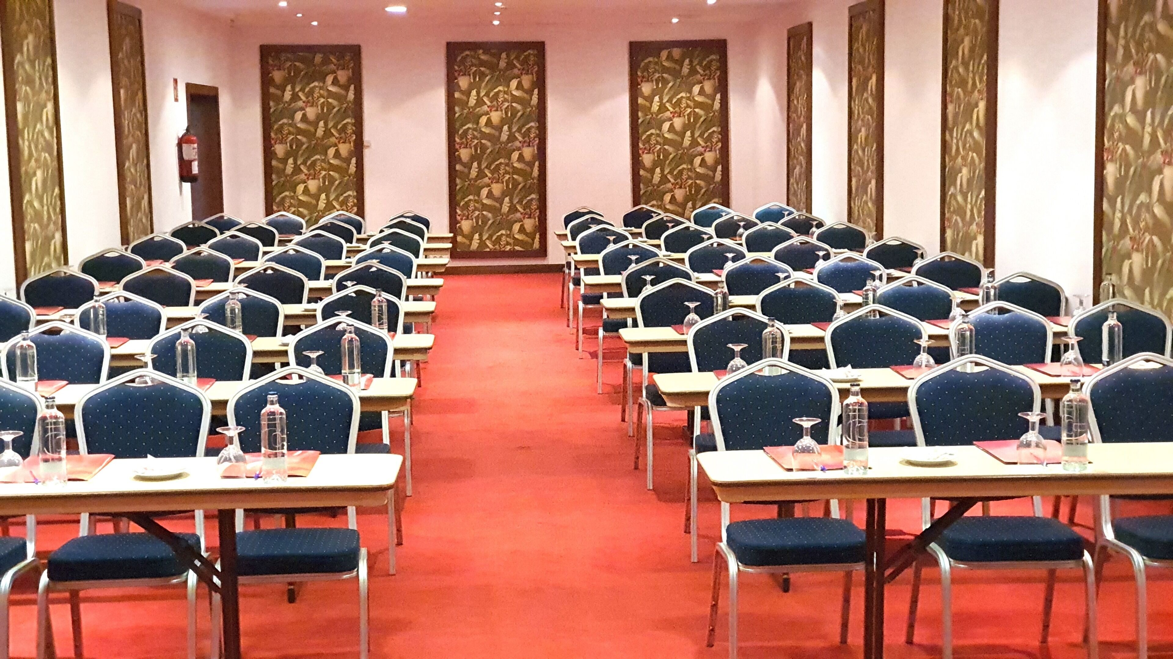 A conference room with rows of tables and chairs, a red carpet, and decorative wall panels.