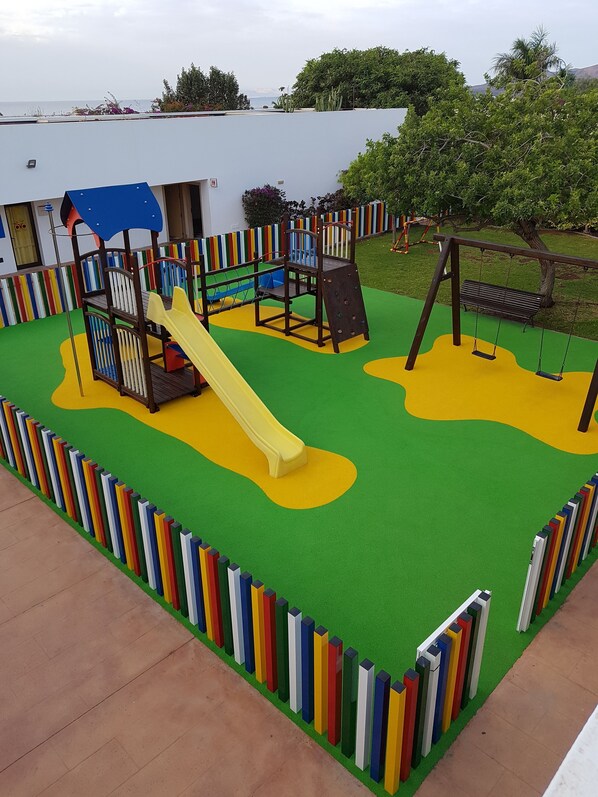 Un espace de jeux pour enfants avec un toboggan, des structures d’escalade et une balançoire.