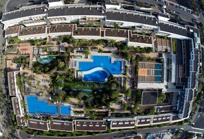 Eine Luftaufnahme eines Resorts mit mehreren Schwimmbecken, Liegestühlen und Palmen.