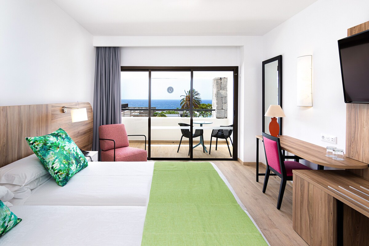 Une chambre d’hôtel avec un lit, un bureau, une chaise et un balcon donnant sur la mer.