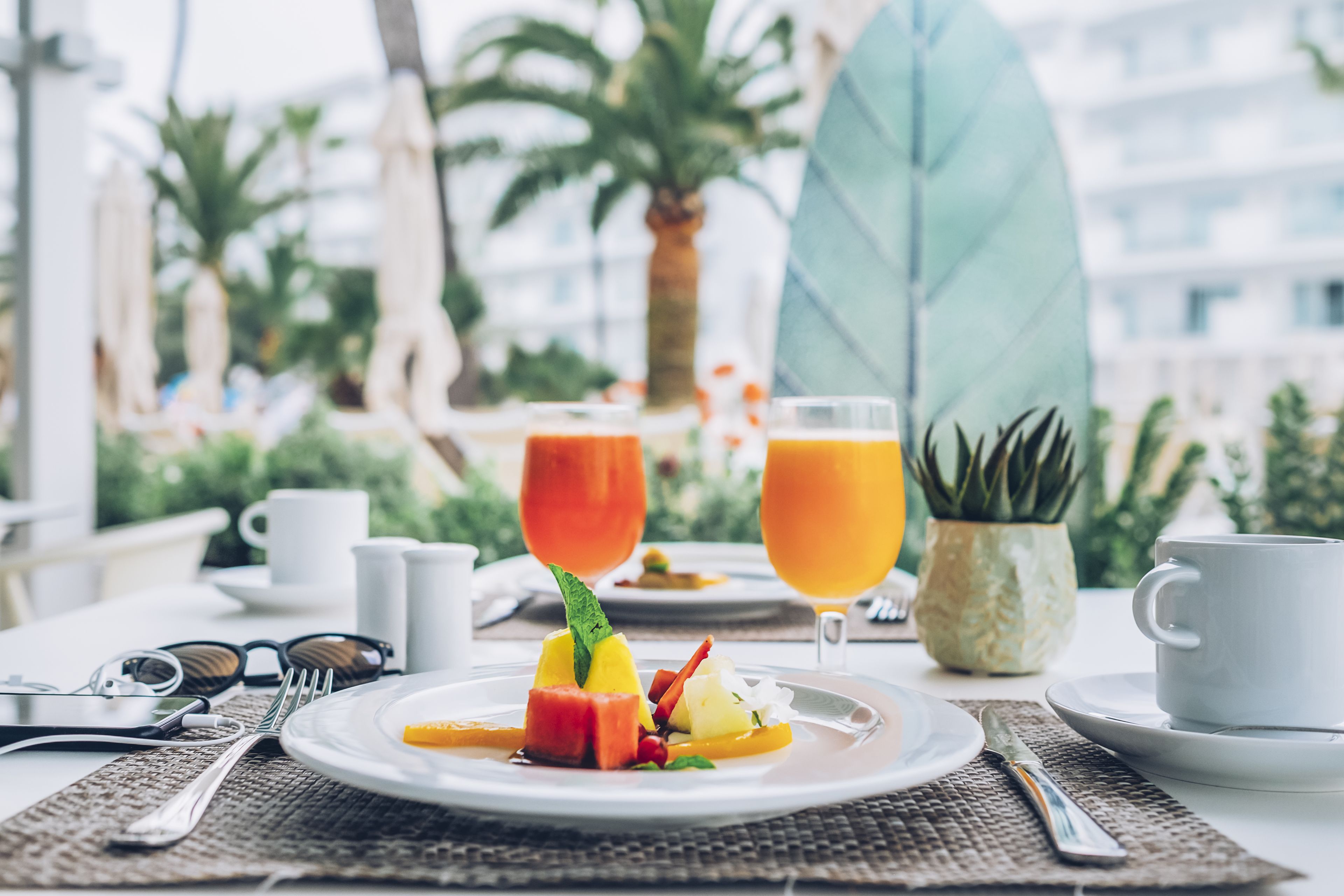 Una mesa de comedor con un plato de fruta, dos vasos de jugo de naranja y una taza de café.