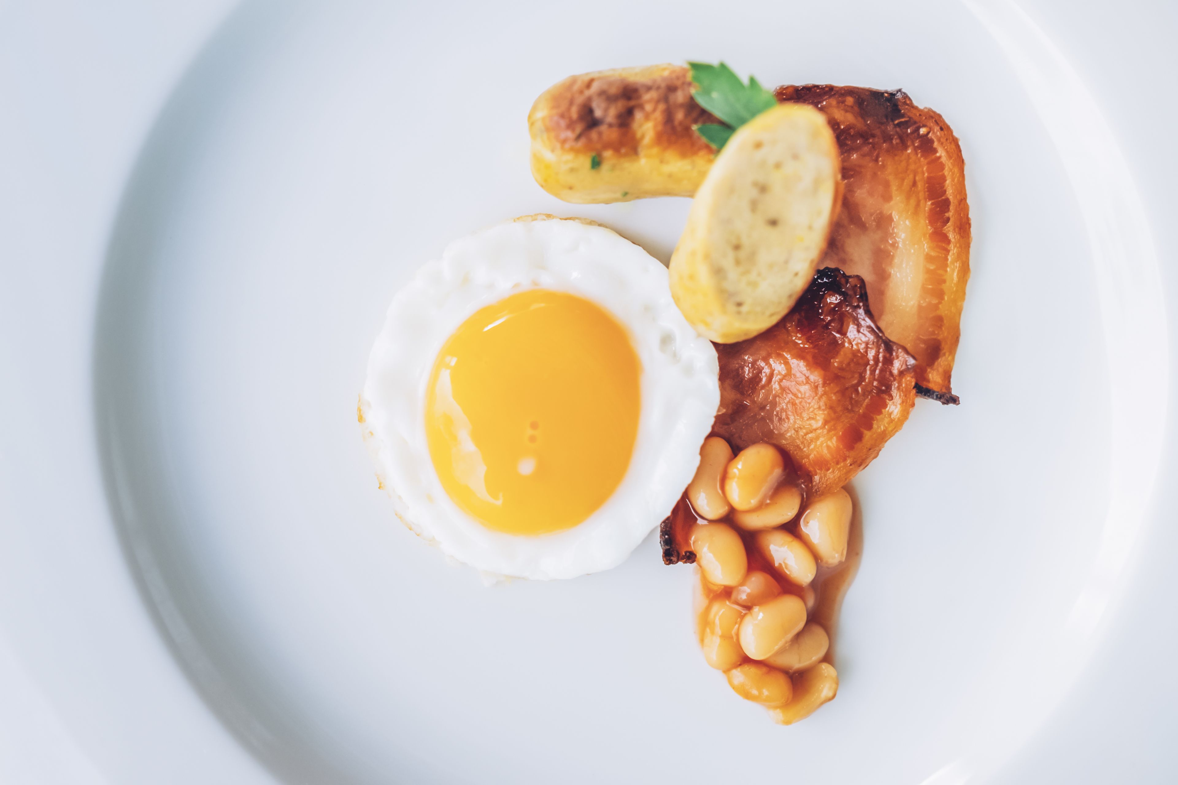 A plate with a fried egg, bacon, beans, and a sausage.