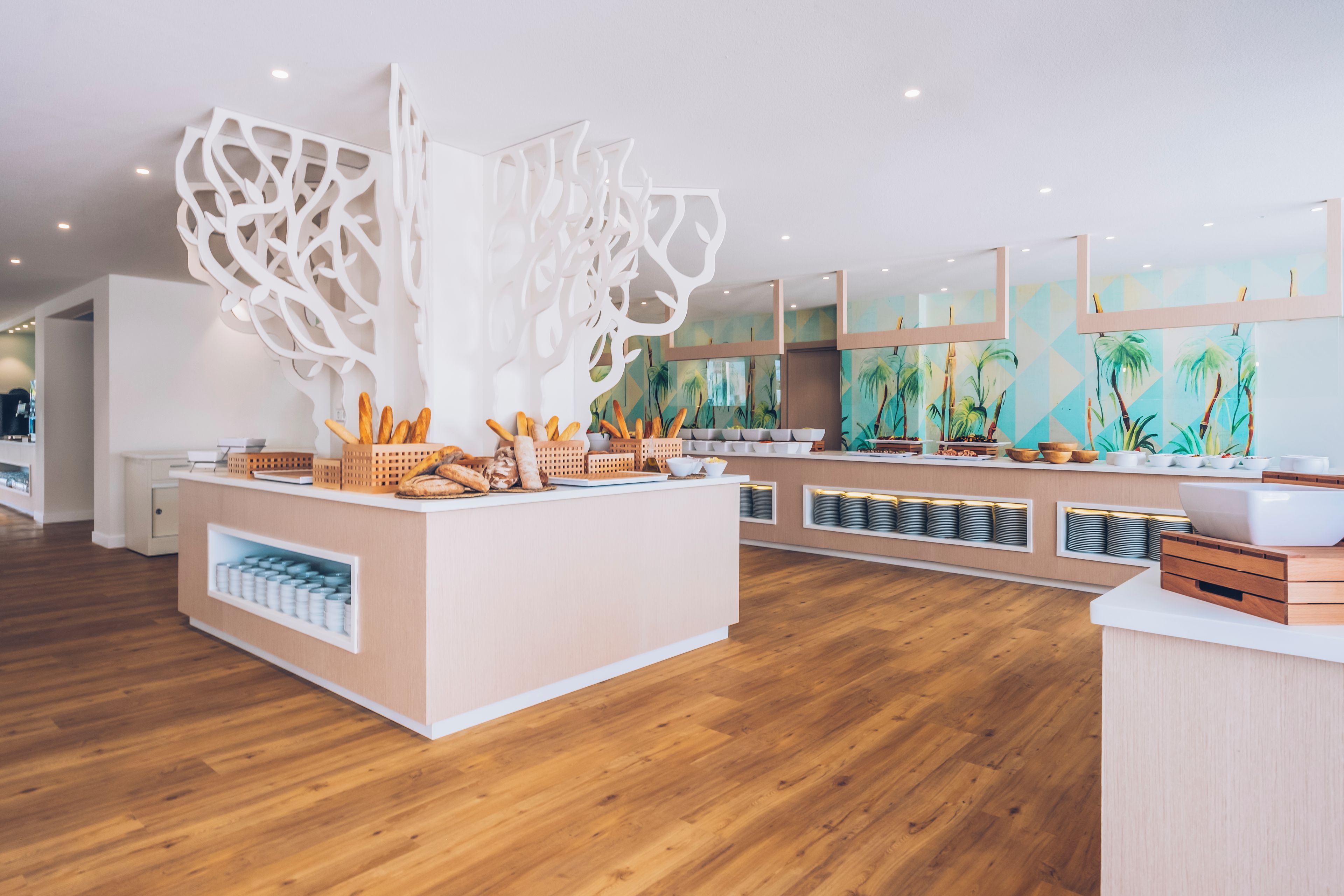 A modern kitchen with wooden flooring, a central island with bread and pastries, and a decorative white partition.