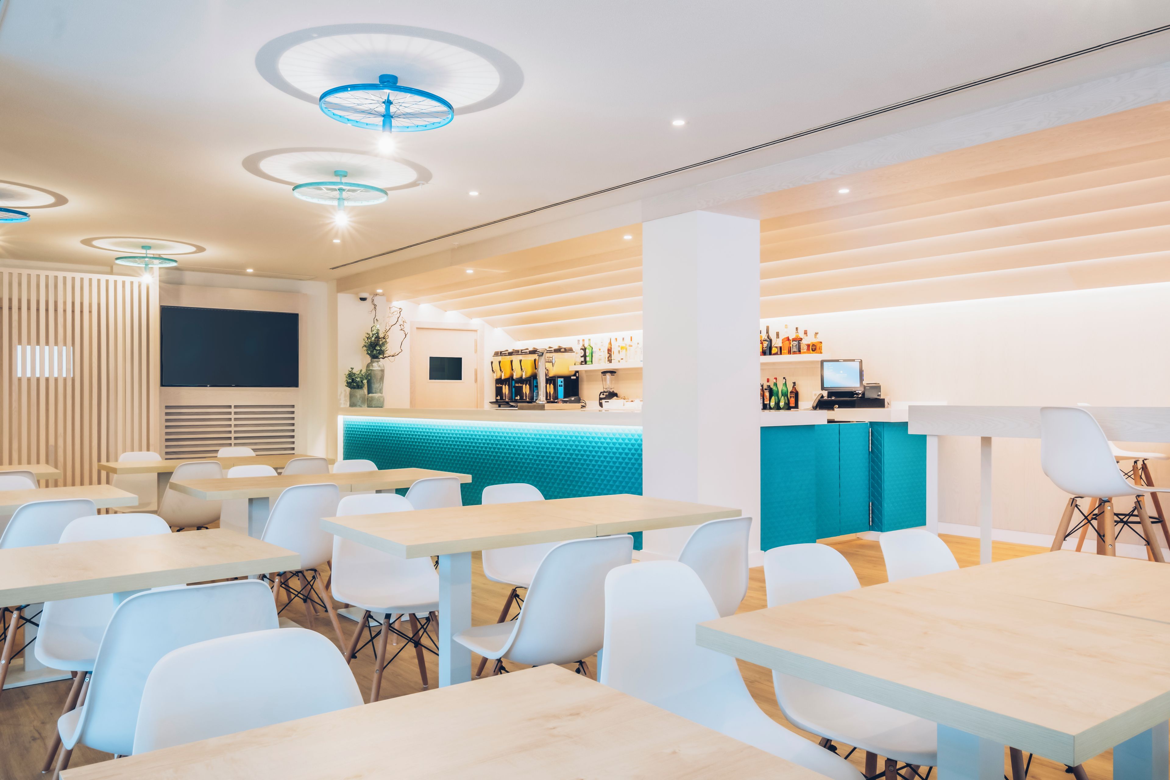 Interior modern d'un restaurant amb taules i cadires de fusta, zona de bar i secció de seients amb un mur amb almofadats blaus.