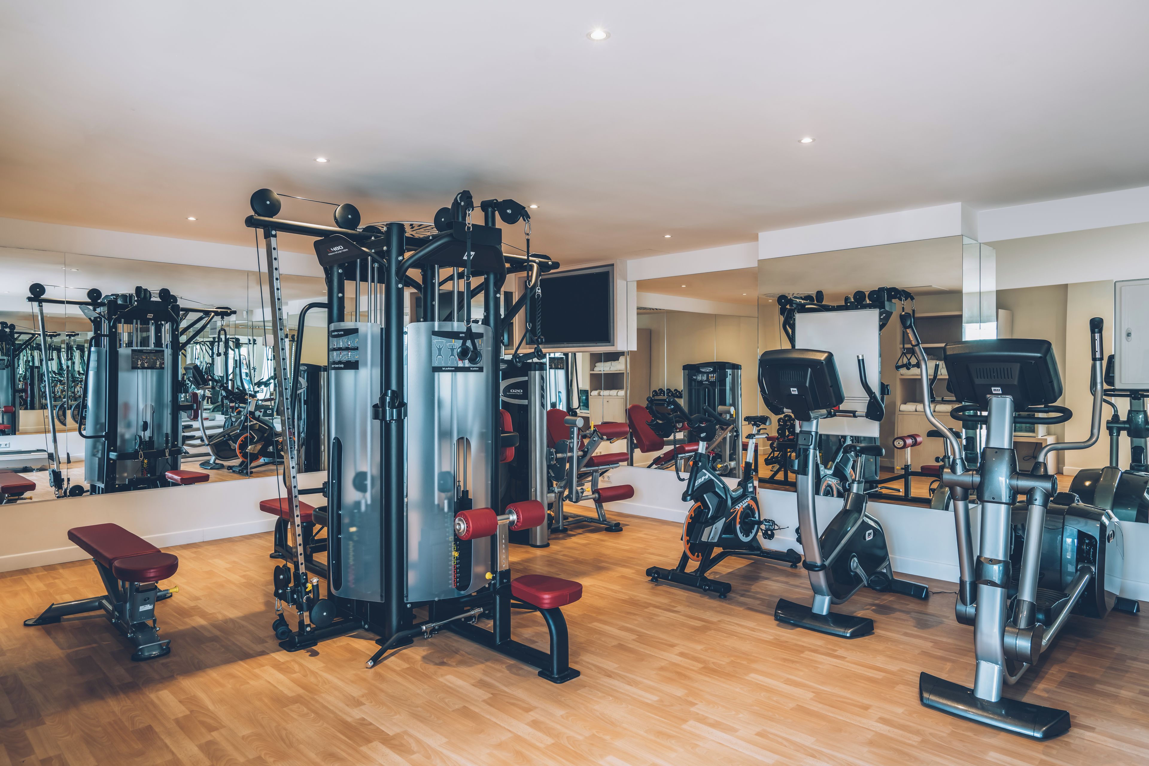 Un gimnasio con diferentes máquinas de ejercicio, espejos y un televisor en la pared.