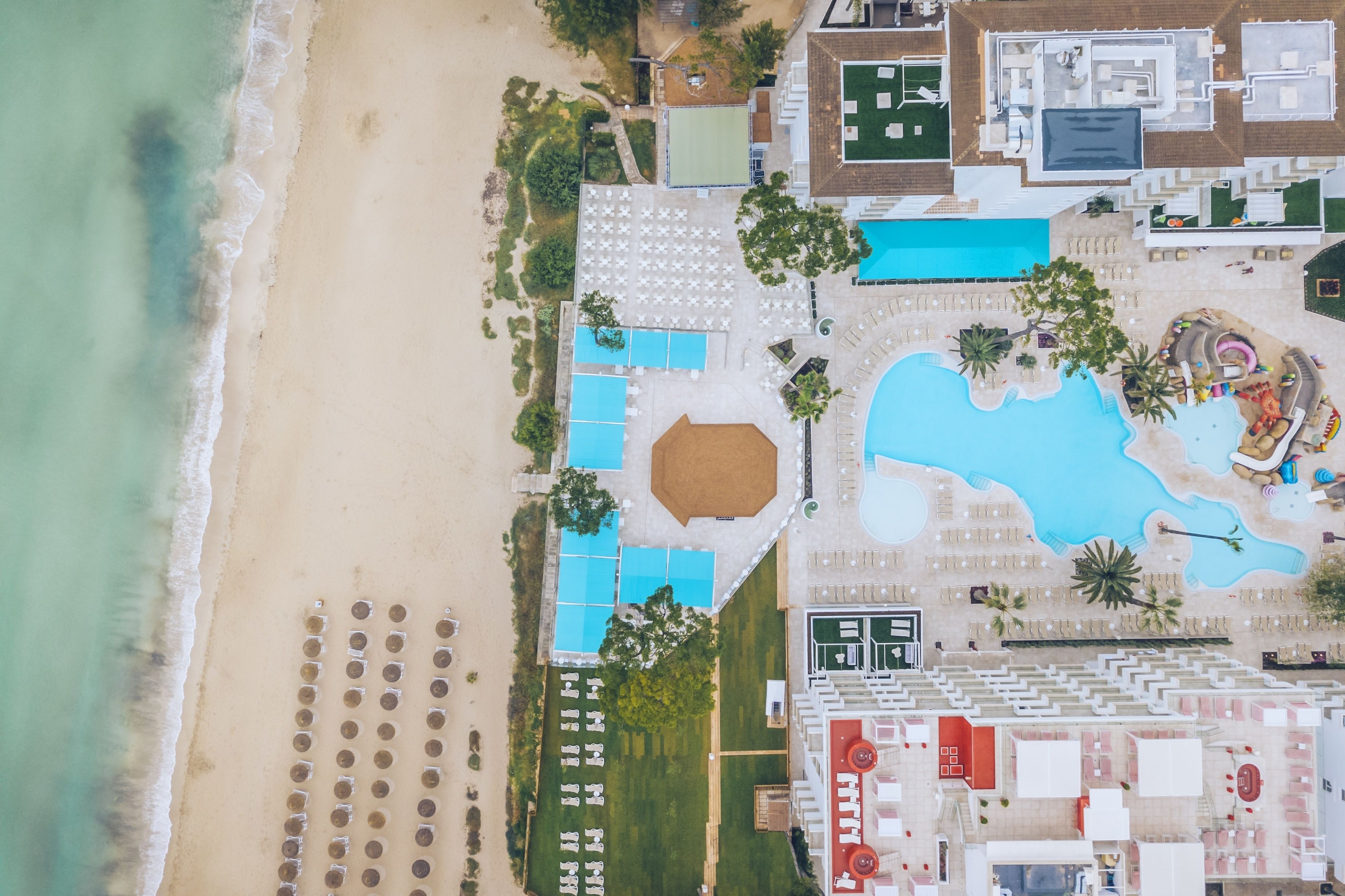 Eine Luftaufnahme eines Resorts mit großem Pool, Strandbereich und mehreren Gebäuden.