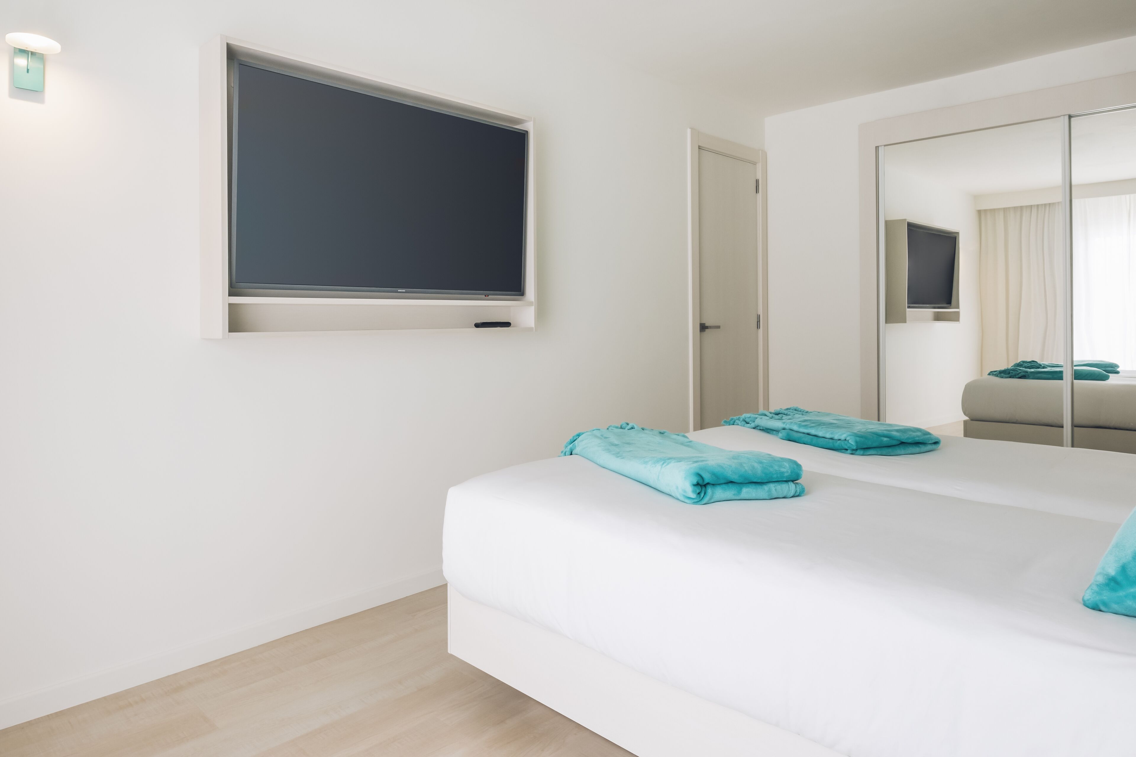 Ein modernes Hotelzimmer mit einem großen Bett, einem flachbildfernseher an der Wand, einem Spiegel und einer Tür zu einem Badezimmer.