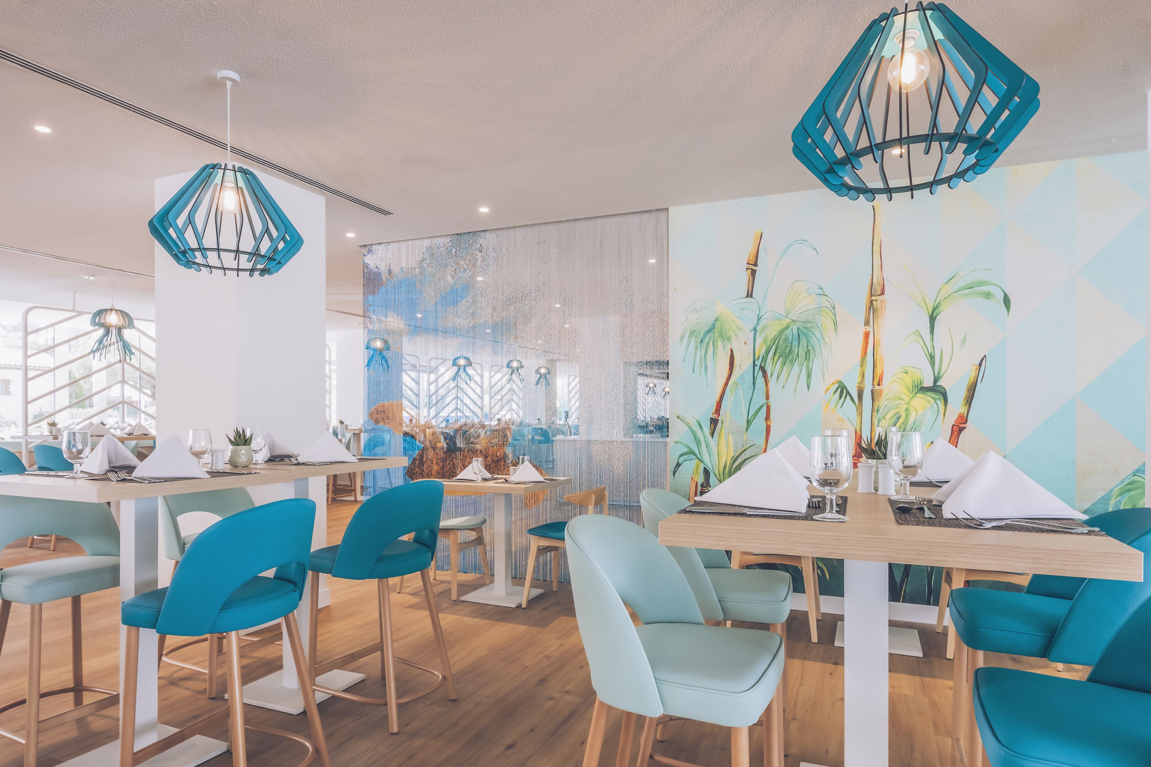 Un restaurante moderno con sillas color turquesa, mesas de madera y arte mural geométrico.