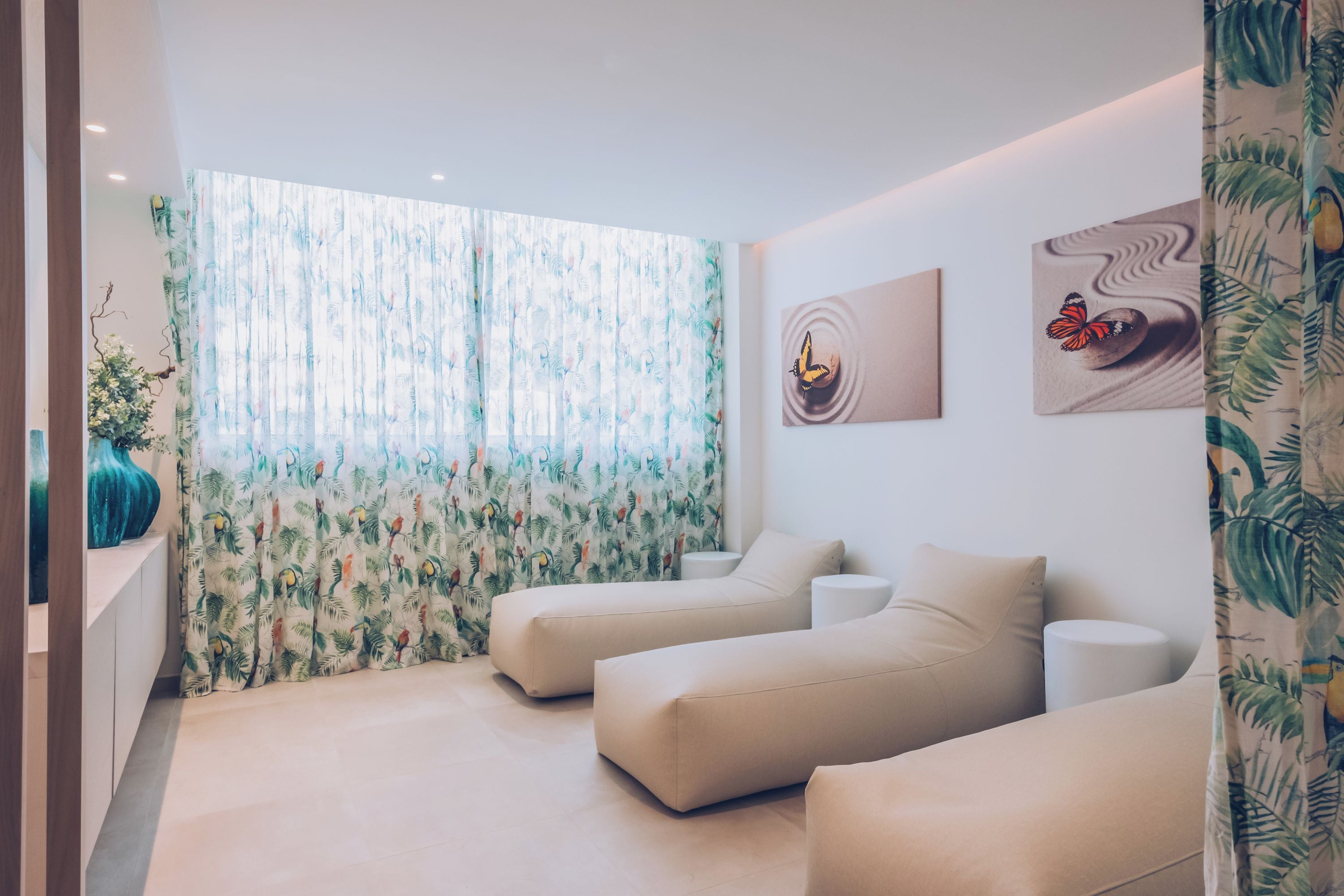 A room with two massage chairs, a large window with curtains, and wall art.