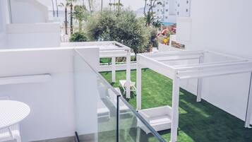 Een modern buitenverblijf met witte meubels, een glazen balustrade en een groen kunstgrasveld.