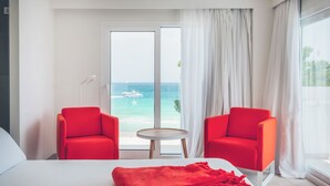 A hotel room with a bed, two red chairs, a small table, and a large window with a view of the sea and a boat. - Iberostar Waves Alcudia Park (Muro)