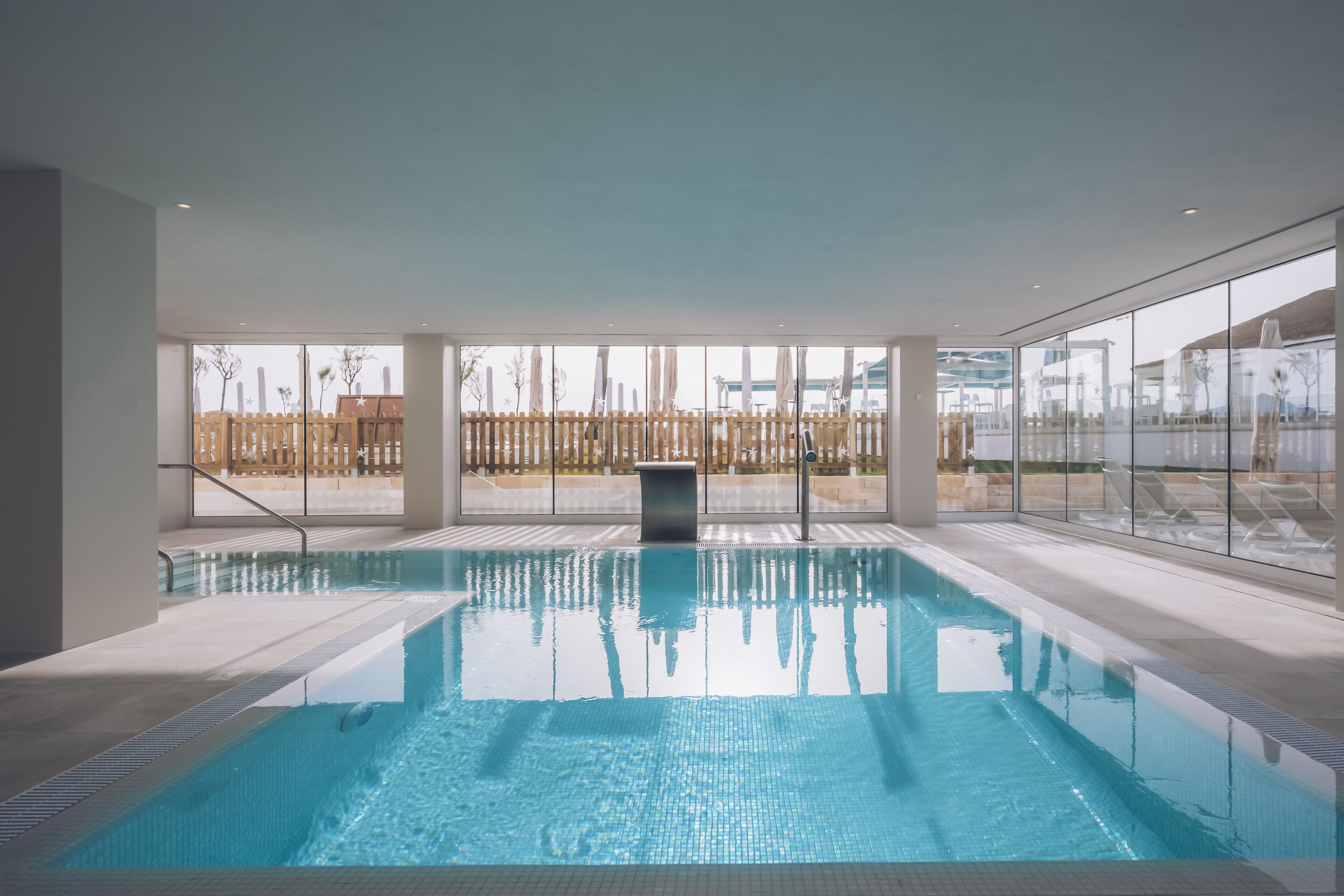 Ein beheiztes Hallenbad mit großen Glaswänden, einer Holzumzäunung und modernem Architekturstil.