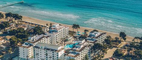 An aerial view of a coastal hotel with multiple buildings, a beach, and a pier.