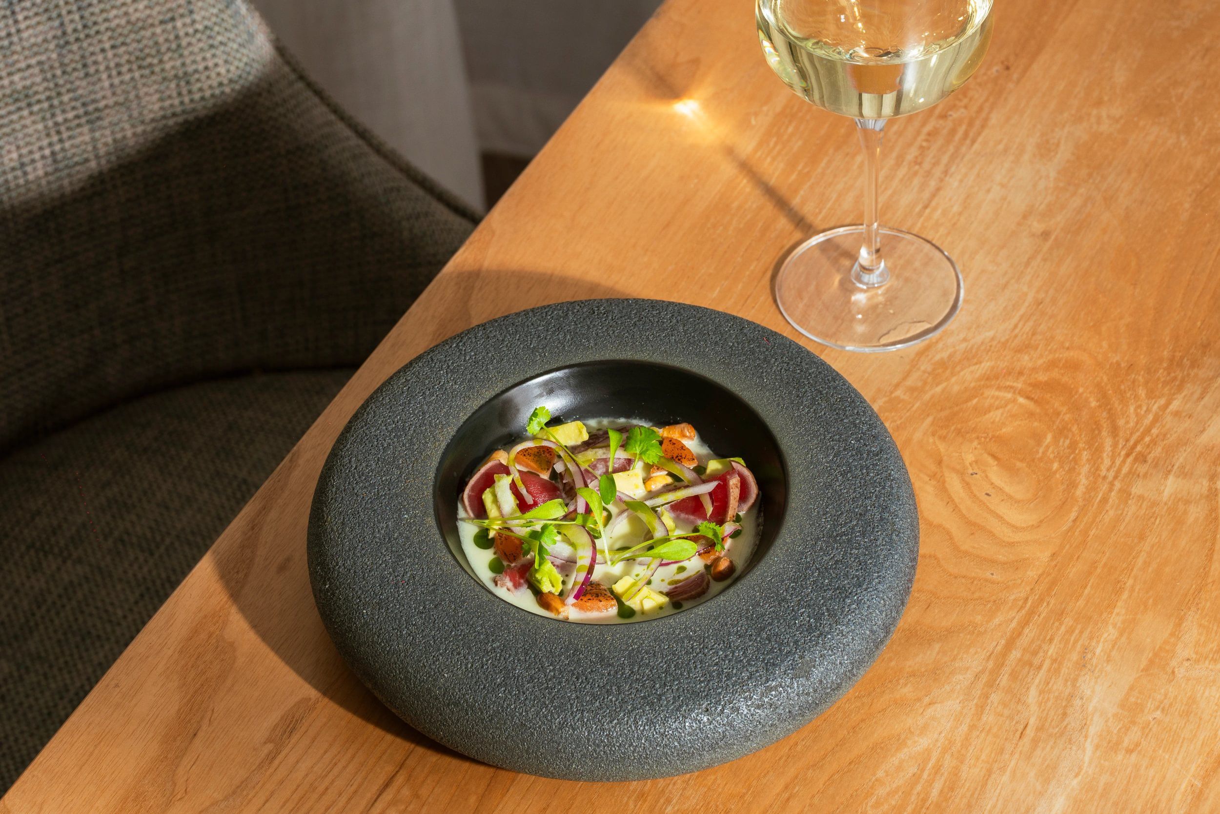 A bowl of food on a wooden table with a glass of white wine beside it.
