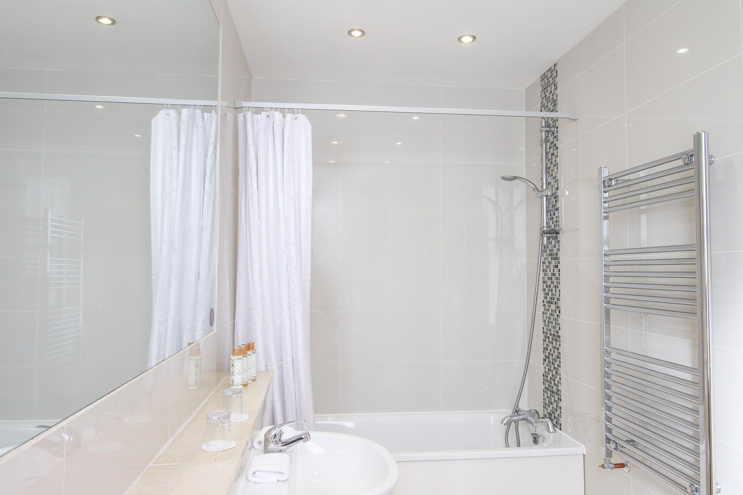 A modern bathroom with a glass shower enclosure, a white sink, and a chrome towel rack.