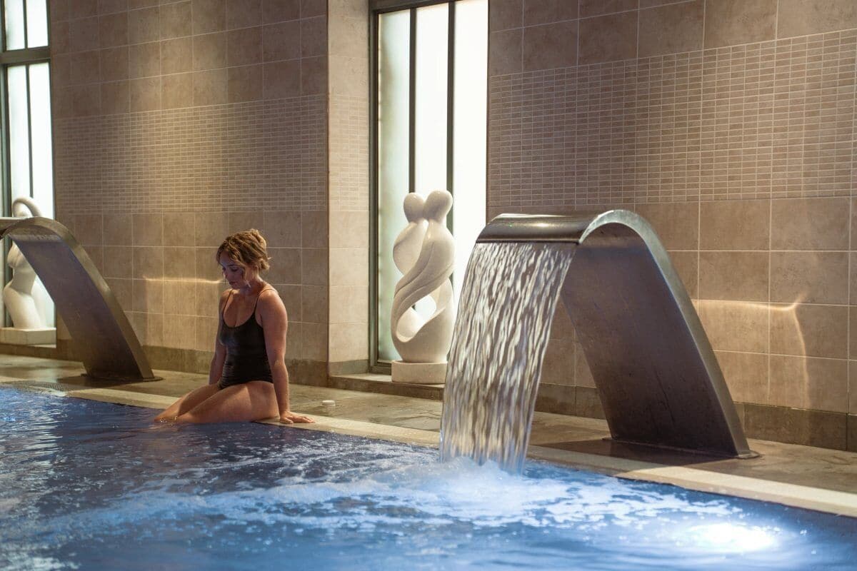 Une personne assise au bord d’une piscine agrémentée d’un élément décoratif aquatique.