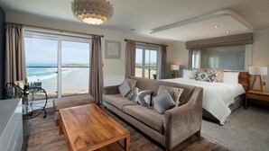 Ein modernes Hotelzimmer mit einem großen Bett, einer Couch, einem Holztisch und Blick auf den Strand.
