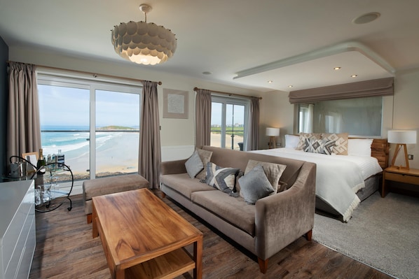 Een moderne hotelkamer met een groot bed, een bank, een houten bijzettafeltje en uitzicht op het strand.