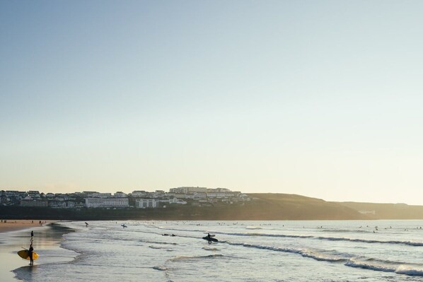 A beach with waves, a surfer, and buildings in the background.