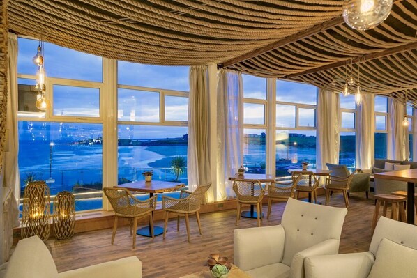 A room with large windows, wicker furniture, and hanging light fixtures. - Fistral Beach Hotel and Spa - Adults Only (Newquay)