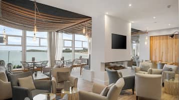 A modern living room with a large window overlooking a body of water, furnished with sofas and a flat-screen TV.