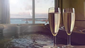 Dos copas de champán sobre una mesa, con un jacuzzi al fondo y vista al mar a través de una ventana.